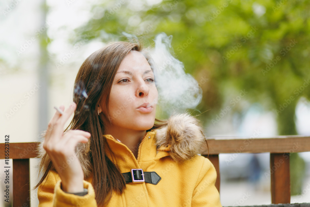 Beautiful happy caucasian young smiling brown-hair woman in yellow coat smoking  cigarette in outdoor restaurant or cafe in autumn season. Rest, smoke,  relax. Stock Photo | Adobe Stock