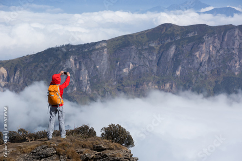Successful woman backpacker taking selfie on mountain peak cliff edge