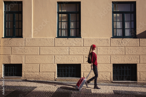 Traveler girl walking in European city with red suitcase