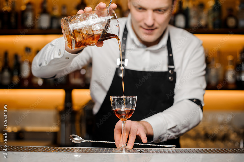 Young bartender pouring alcoholic drink into a glass