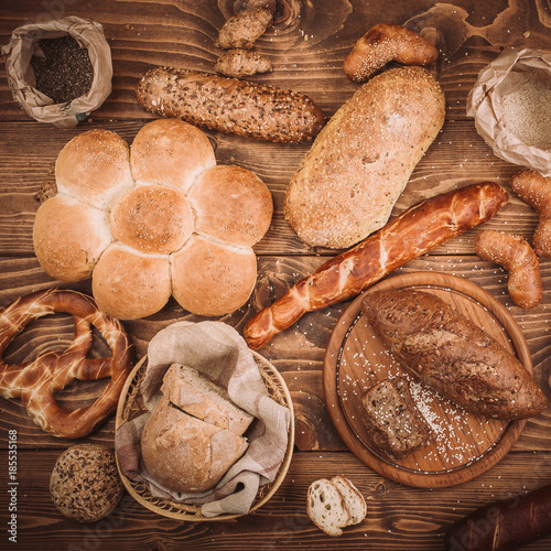 Many mixed baked breads and rolls on rustic wooden table