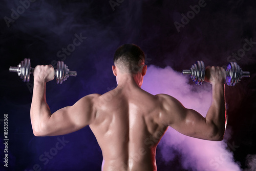 Muscular young bodybuilder with dumbbells in colorful smoke © Africa Studio