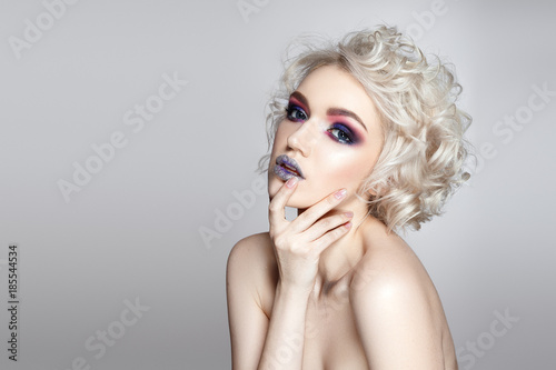 Beautiful woman portrait on grey background with violet and silver glamour make up and curly hair.