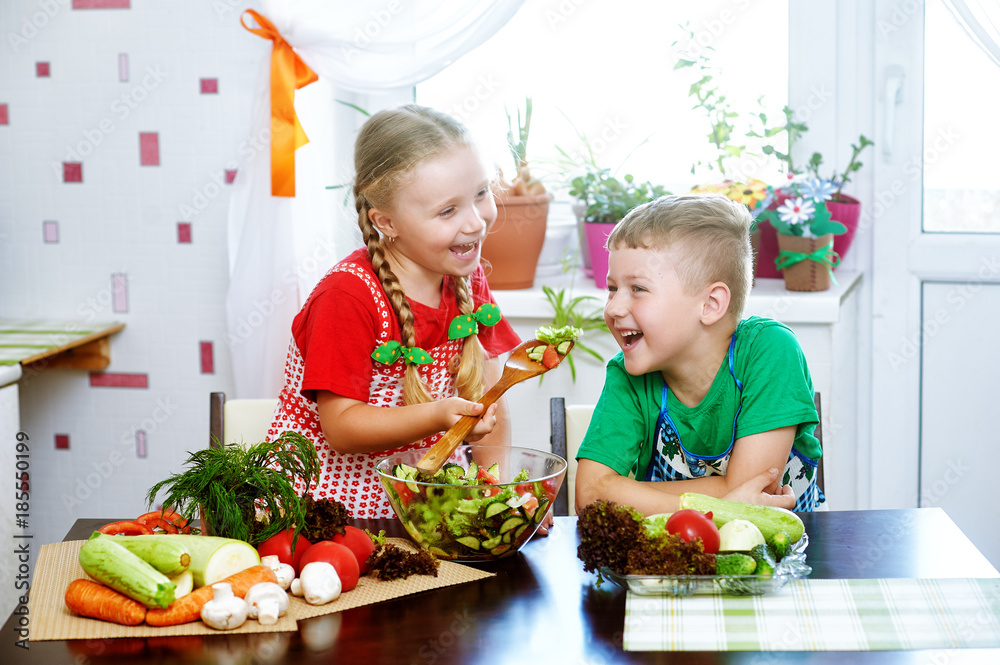 Fun children prepare salad vegetables . Happy kids in the kitchen . The concept of a healthy vegetarian diet