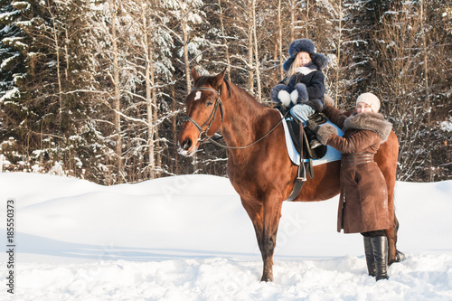 Small girl and mom near horse in a winter © keleny