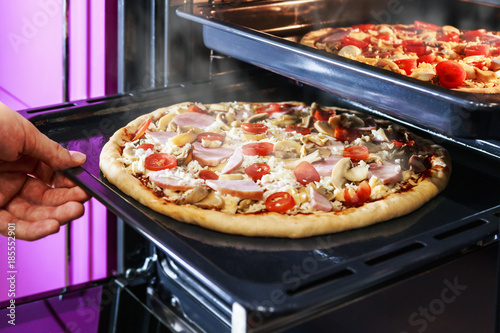 hand moves the tray of pizza with mushrooms, ham and mozzarella cooked baking in the oven. 