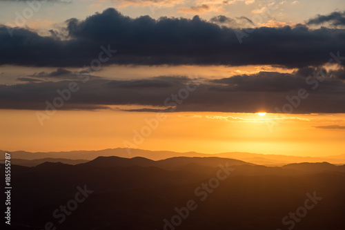 Sunset over mountains range in Umbria, with sun coming down behind some clouds © Massimo