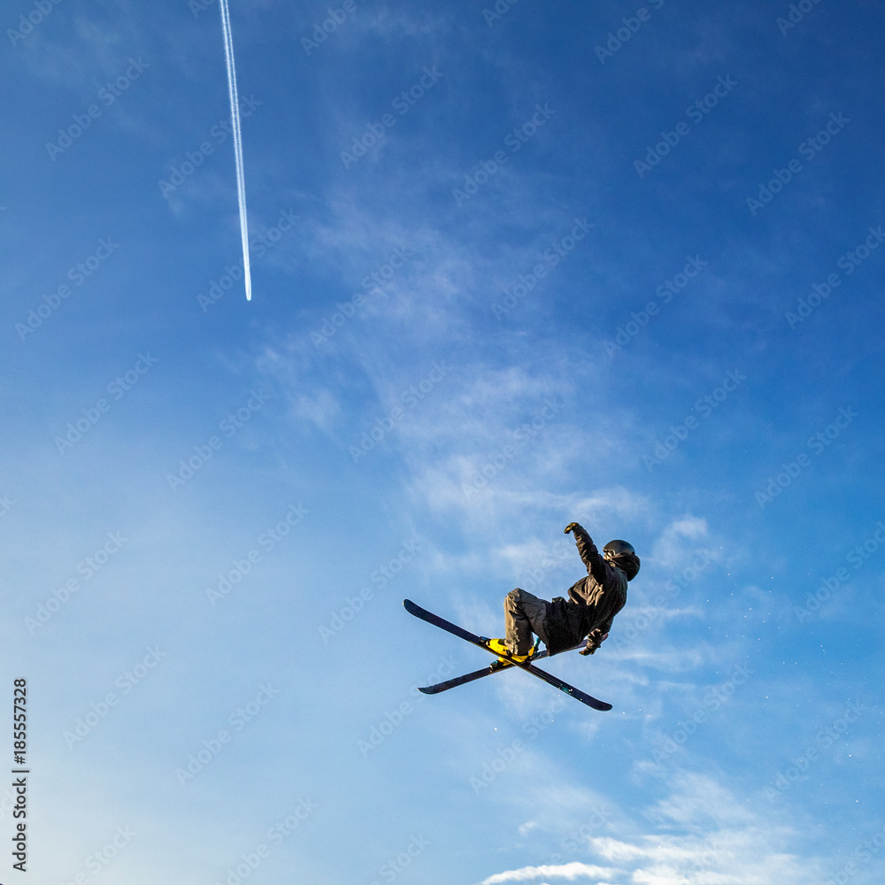 Ski jumper flying high in the air on a blue sky background with a trace of a jet aircraft. Ski jumper flying high in the air on a blue sky background with a trace of a jet aircraft.