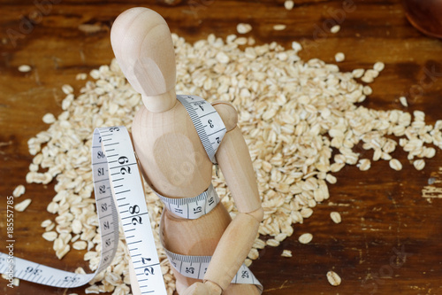 Wooden dummy is strapped with tape measure with pile of rolled oat in the background. Concept of weight loss and management