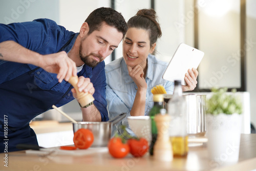 Couple cooking in kitchen, reading recipe on tablet