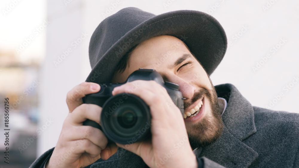 Closeup of happy paparazzi man in hat photographing celebrities on camera and smiling outdoors