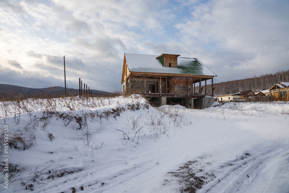 Abandoned unfinished house stands on a snow-covered hill.