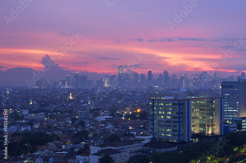 The scenery of Jakarta city in the evening with the sparkling lights of buildings and houses of residents, decorated with a reddish sky.