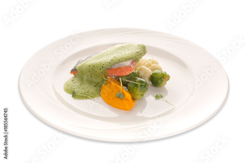 Red fish and vegetables under a frothy sauce on an isolated background