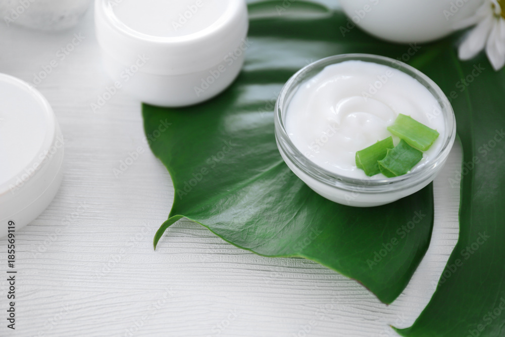 Bowl with body cream and aloe leaves on table