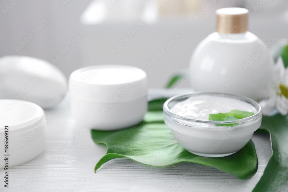 Bowl with body cream and aloe leaves on table