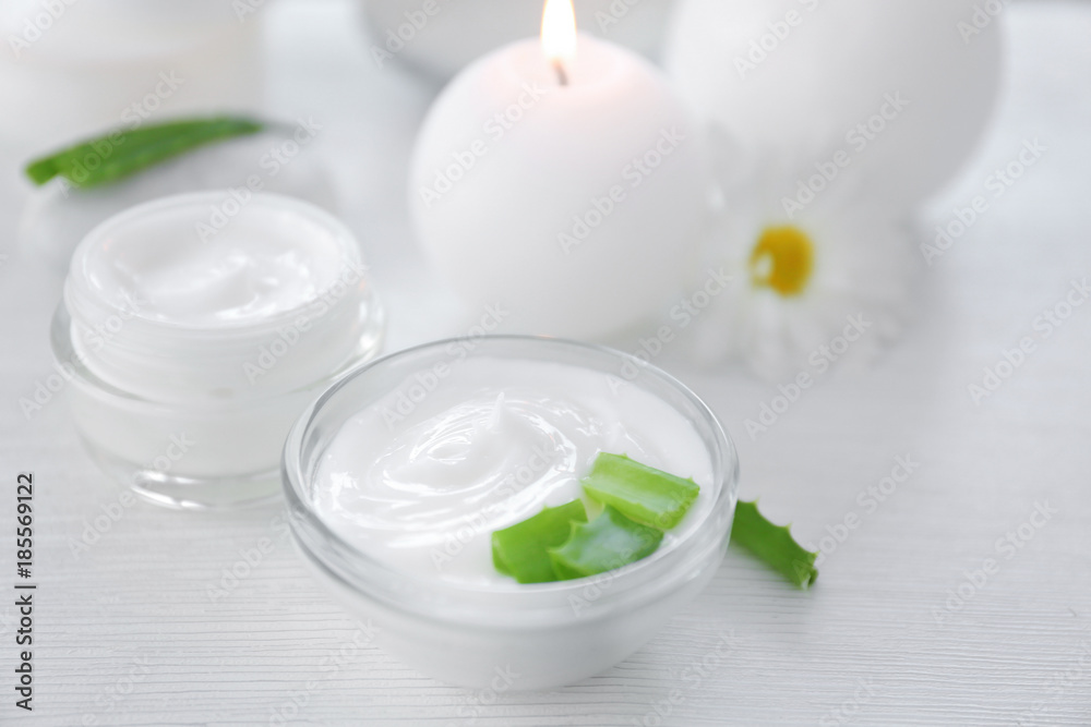 Bowl with body cream and aloe leaves on table