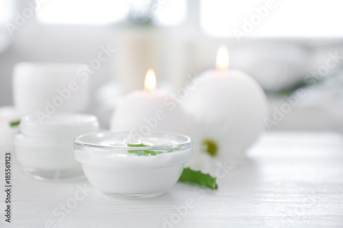 Bowl with body cream and aloe leaves on table
