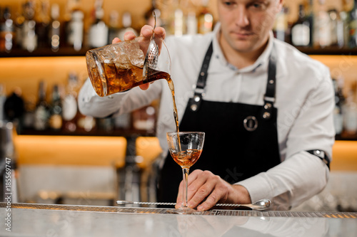 Young barman adding alcoholic drink into an elegant glass
