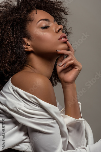 Young tender african american woman in white shirt dreaming with hand on chin isolated on grey background