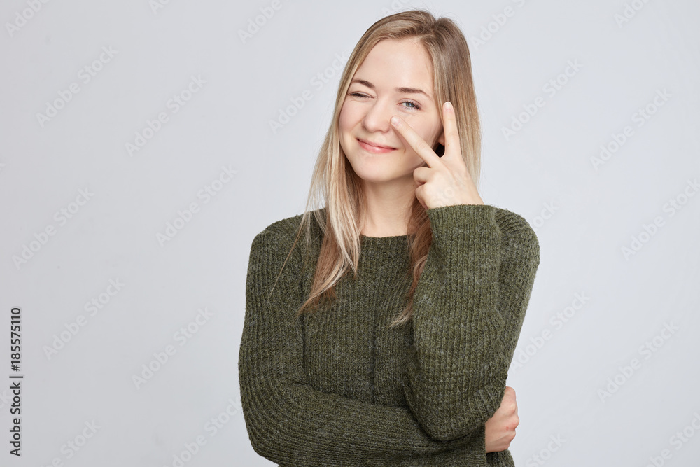 Close up isolated studio portrait of young blonde Caucasian female smiling and looking at the camera through her fingers in i'm watching you gesture. Human face expressions and emotions, body language Close up isolated studio portrait of young blonde Caucasian female smiling and looking at the camera through her fingers in i'm watching you gesture. Human face expressions and emotions, body language