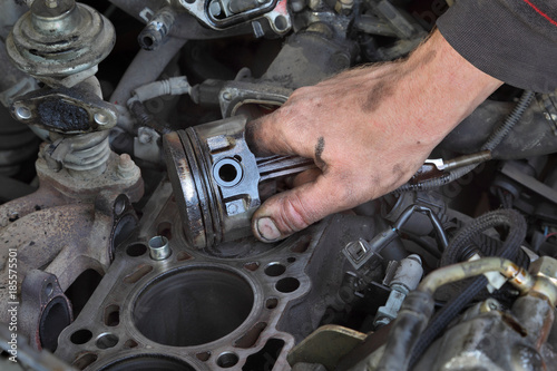 Car mechanic holding old piston at engine after disassembly, part replacing