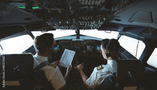 Pilot and copilot looking at instruction list in airplane photo
