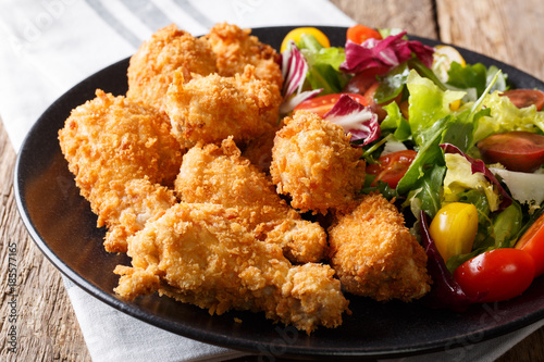 Canvastavla deep-fried chicken wings in breadcrumbs and fresh salad close-up on a plate