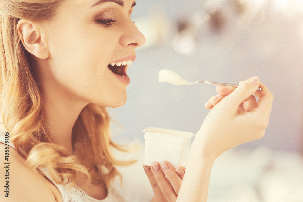 One more spoon. Positive delighetd woman eating joghurt and expressing joy while smiling One more spoon. Positive delighetd woman eating joghurt and expressing joy while smiling