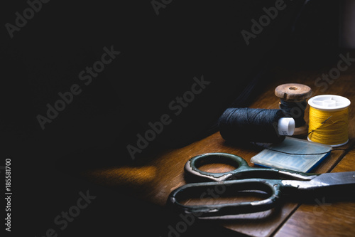 Old sewing machine with black thread scissors and needle, on a old grungy work table. Tailor's work table. textile or fine cloth making. industrial fabric