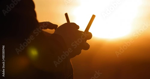 Close view of pilot's hands with remote control as he flies a drone at sunset. Strongly backlit with silhouette and lens flares. Hand-held real-time 4K.