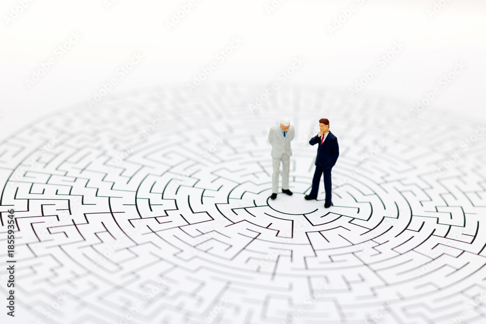 Miniature people: Businessman standing on center of maze. Concepts of finding a solution, problem solving and challenge. Miniature people: Businessman standing on center of maze. Concepts of finding a solution, problem solving and challenge.