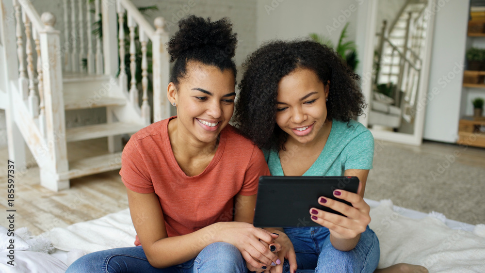 Cheerful mixed race young funny girls talking online video chat on tablet computer with their friends at home Cheerful mixed race young funny girls talking online video chat on tablet computer with their friends at home