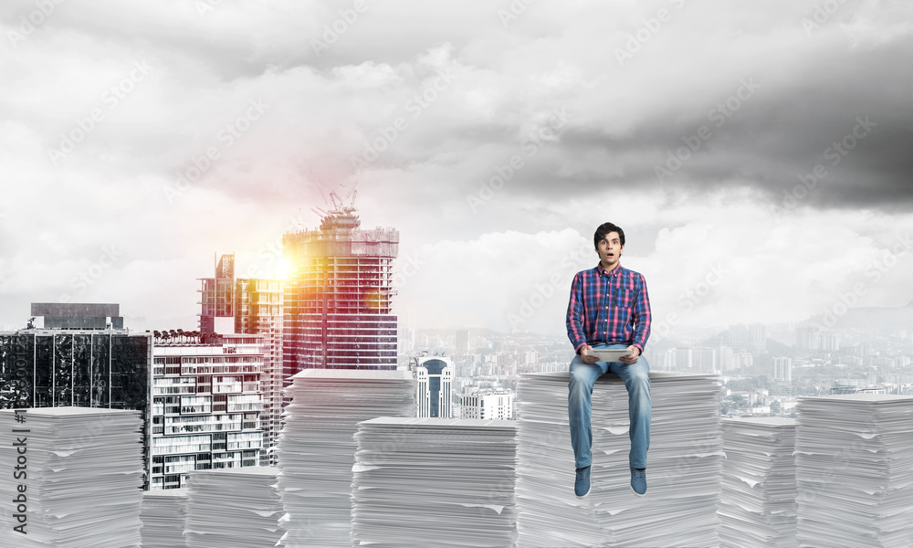 Attractive man sitting on pile of paper documents.