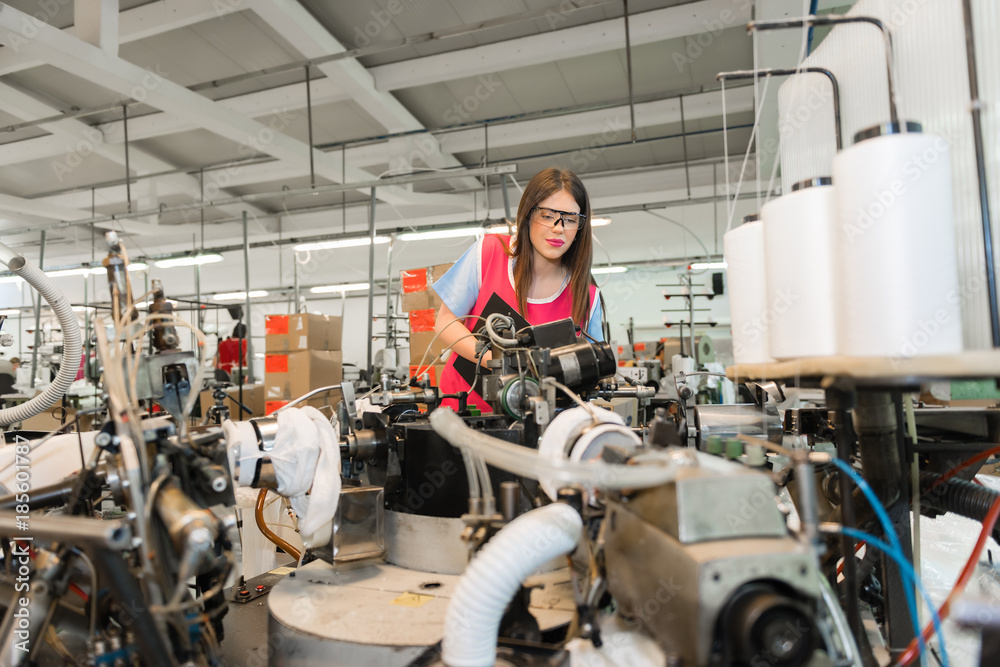 Young woman controlling automated production of textile thread and cotton spinning