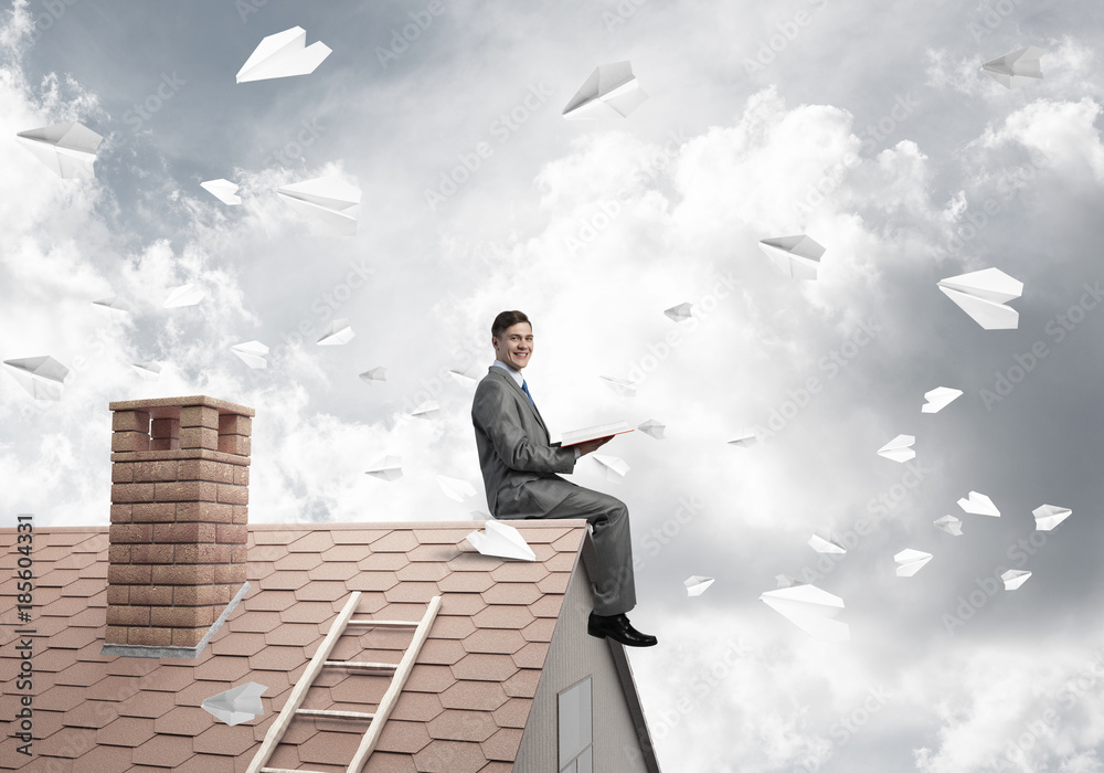 Man on brick roof reading book and paper planes flying in air Man on brick roof reading book and paper planes flying in air