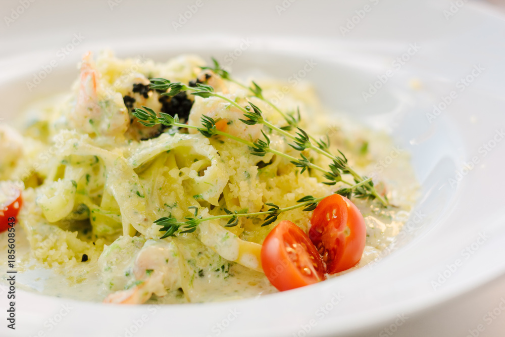 Close up view of italian fettuccine pasta with pesto sauce and cherry tomatoes.