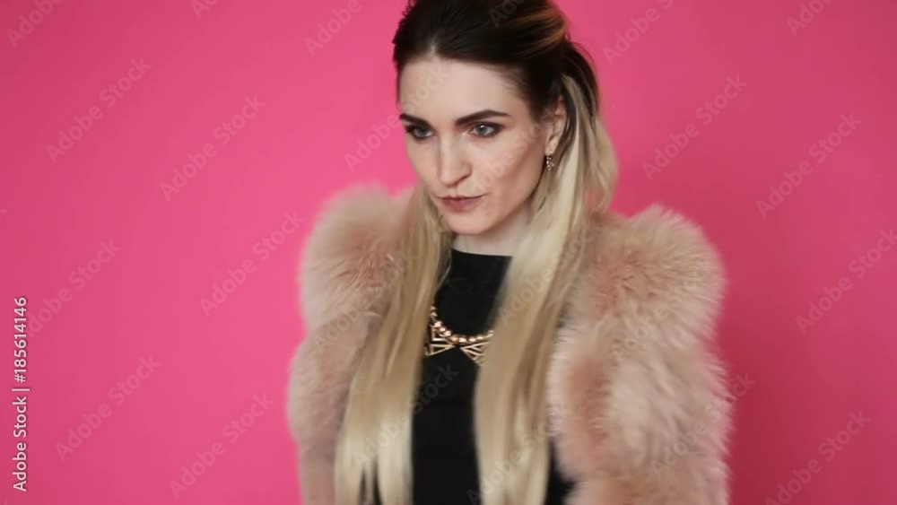 Beautiful girl with long dyed hair in a beautiful fur coat is dancing on pink background. Beautiful girl with long dyed hair in a beautiful fur coat is dancing on pink background.