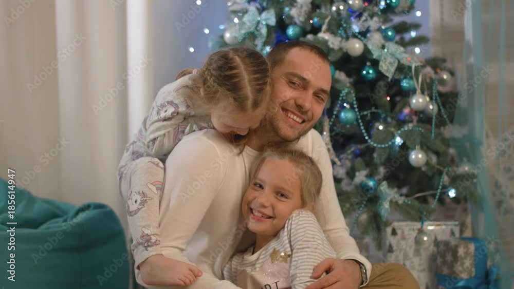 Happy father with two daughters laughing, playing and hugging near Christmas tree Happy father with two daughters laughing, playing and hugging near Christmas tree