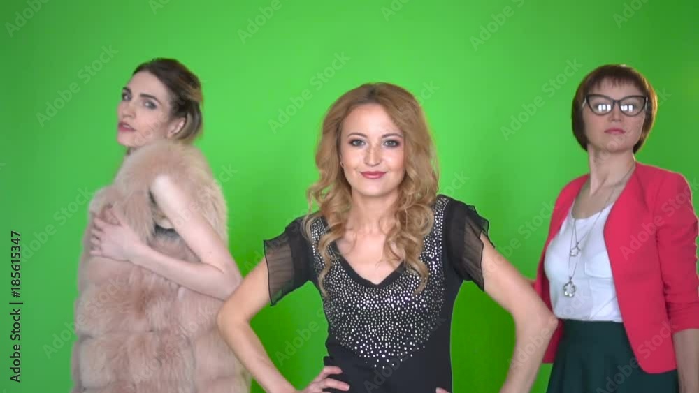 Three beautiful young women in stylish clothes dansing at camera on green screen background