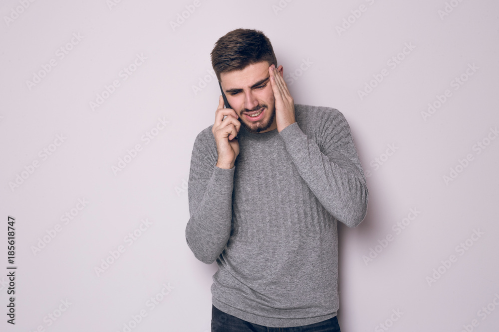 Portrait of a puzzled businessman in gray sweater standing and talking on mobile phone isolated over gray background Portrait of a puzzled businessman in gray sweater standing and talking on mobile phone isolated over gray background