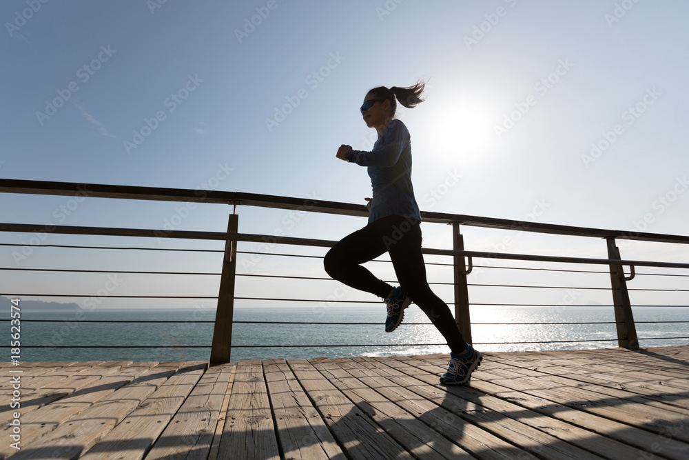 sporty female runner running on seaside boardwalk during sunrise