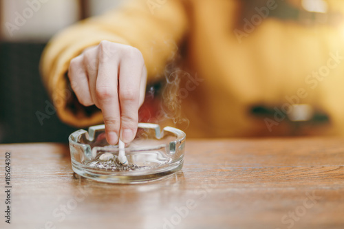 Focus on caucasian young woman hand putting out cigarette on glass ashtray on wooden table, cigarette butt, smoking is dying. Quit smoking. Health concept. Close up photo. photo