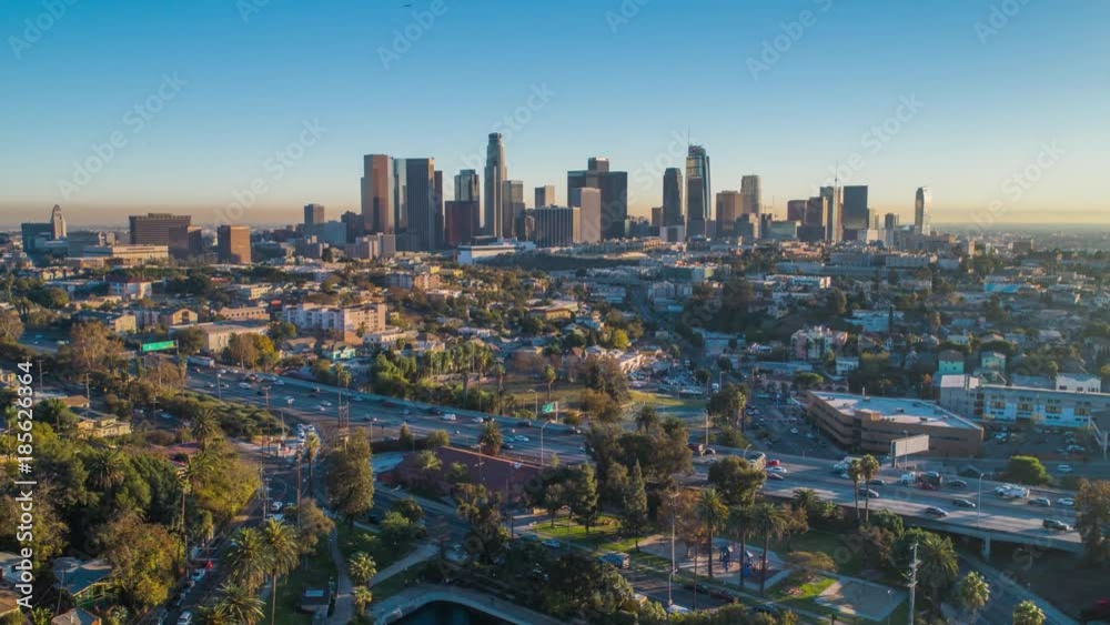 Cinematic urban aerial time lapse of downtown Los Angeles skyline with freeway traffic.