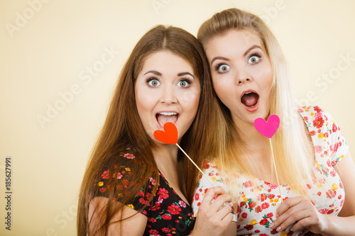 Two happy women holding heart on stick