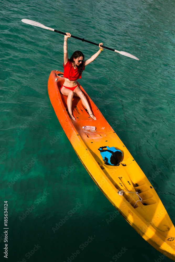 Fototapeta premium Brunette young woman girl in red bikini paddling on red, orange, yellow kayak in the blue water. Asia. Thailand