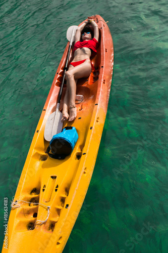 Brunette young woman girl in red bikini lying ,lie on red, orange, yellow kayak in the blue water. Asia. Thailand © Ruslan Full