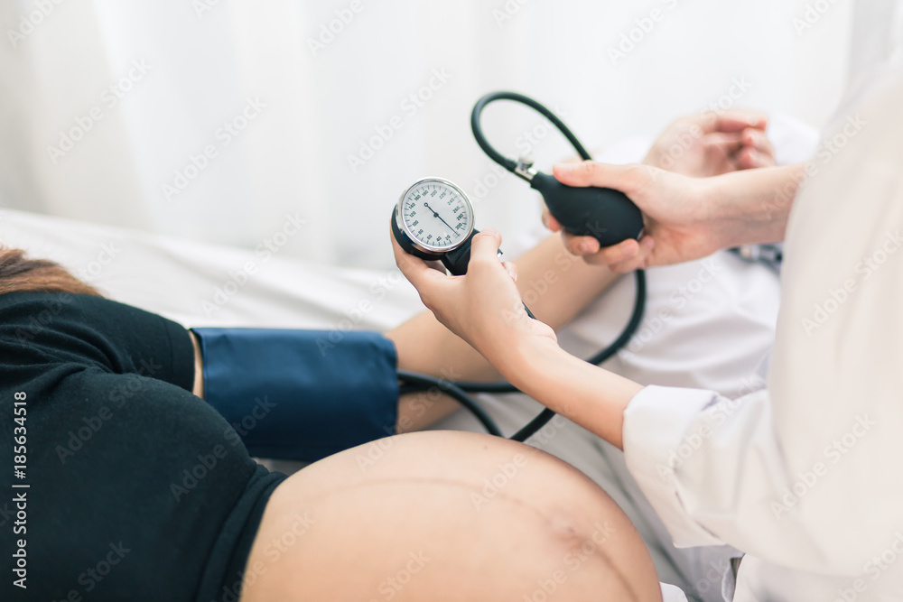 Obraz premium Female Obstetrician doctor measuring blood pressure of the pregnant woman in the hospital. Pregnancy-induced Hypertension concept.