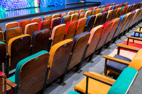 The auditorium in the theater. Multicolored spectator chairs. The stage with scenery and curtains. © Andrey Lapshin
