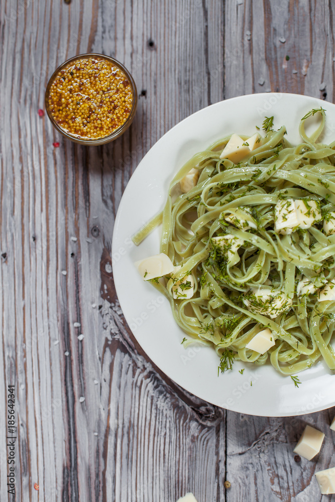 spaghetti with spinach green with mozzarella, herbs and French mustard on a white plate on a light wooden table spaghetti with spinach green with mozzarella, herbs and French mustard on a white plate on a light wooden table